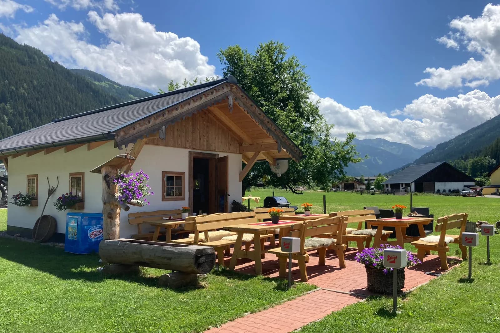 Hütte mit Terrasse und Holzbänken im Garten des Ferienhofs