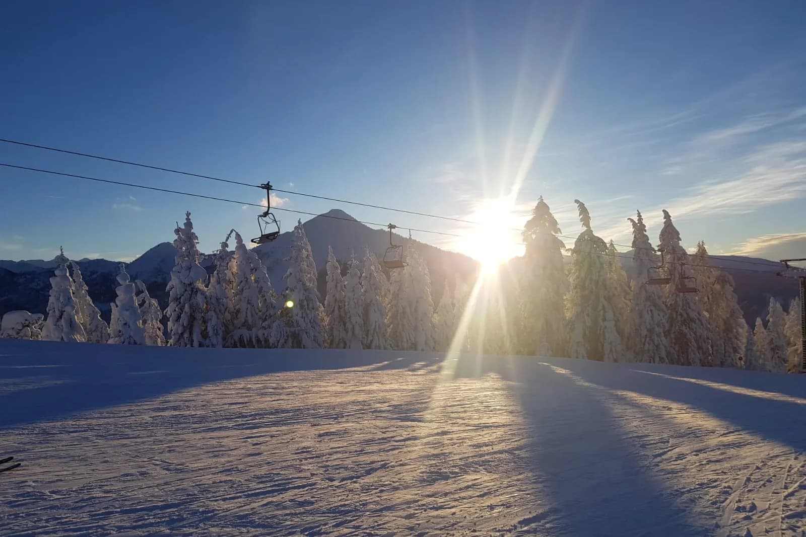 Skipiste mit Sessellift im Gegenlicht der Wintersonne
